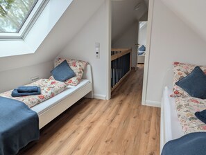 Une chambre de taille modeste, avec deux lits, un plancher en bois et une lucarne.