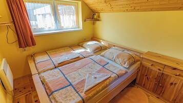 A two-bed room with wooden furniture, a window with curtains, and a wooden ceiling.