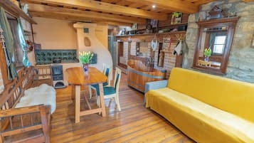 A cozy interior with a wooden dining table, chairs, a yellow sofa, and a stone wall.