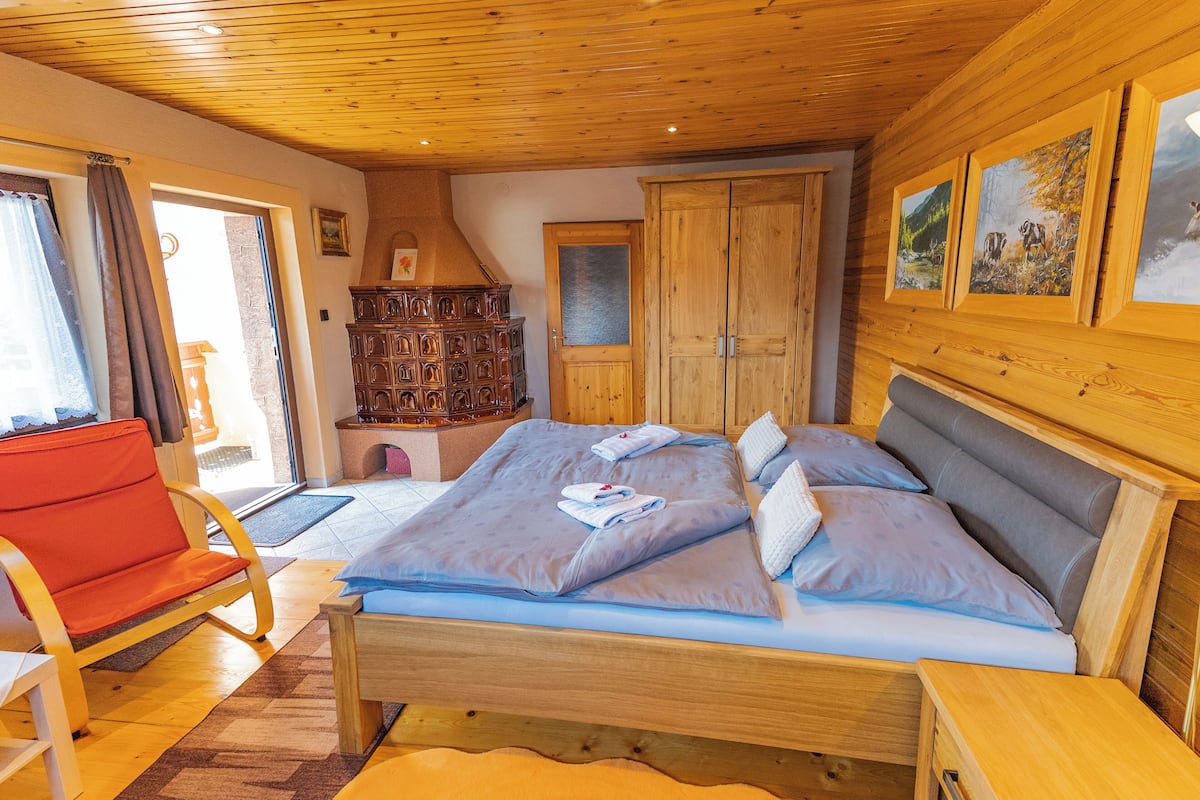 Un lit en bois avec un cadre en bois, recouvert d’une literie bleue, une chaise rouge et une armoire en bois.