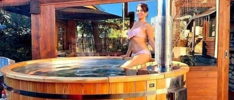 Un jacuzzi con revestimiento de madera, rodeado por una terraza de madera y un área cubierta.