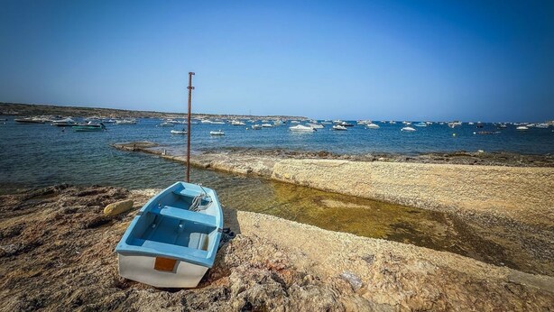 Uma costa rochosa com um barco pequeno atracado à esquerda.