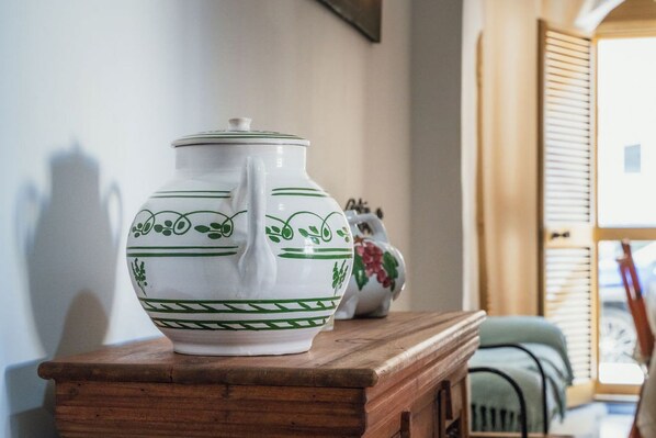 Una jarra de cerámica blanca con diseños verdes sobre una mesa de madera en una habitación con ventana y puerta.