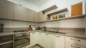 Cozinha compacta com fogão a gás, forno e pia. Há armários e bancada com torradeira e chaleira.