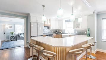 A modern kitchen with a central island, bar stools, pendant lighting, and a view into the living area.
