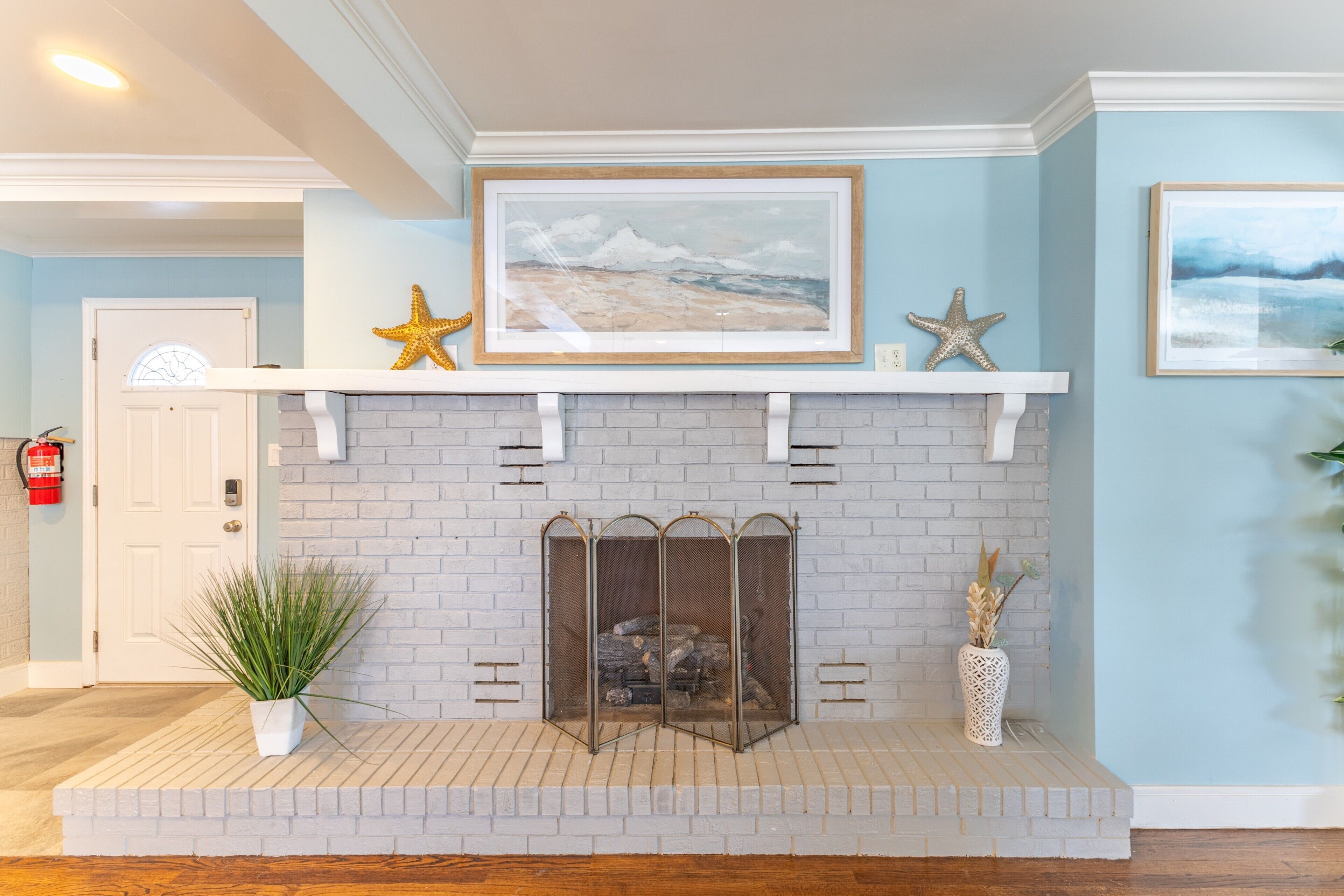 A fireplace with a brick surround, a framed picture above it, and decorative starfish.