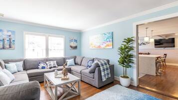 A living room with a grey sofa, a white coffee table, and a blue rug. There is a potted plant and artwork on the walls.