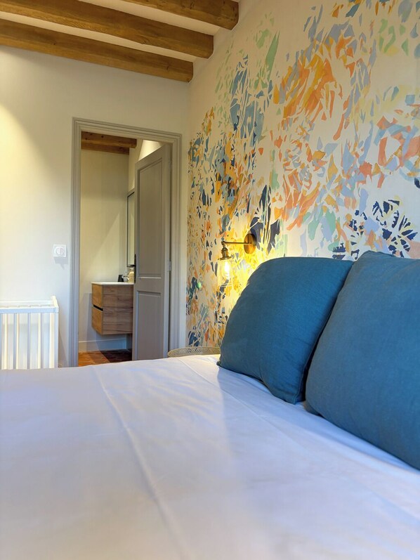 A bedroom with a bed, a wooden ceiling, a wall with abstract art, a nightstand, and a mirror.