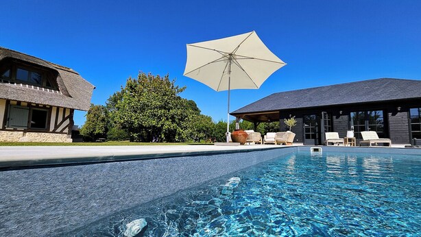 A swimming pool with clear blue water, lounge chairs, and umbrellas.