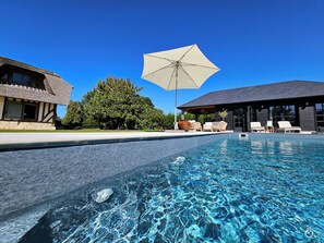 A swimming pool with clear blue water, lounge chairs, and umbrellas.