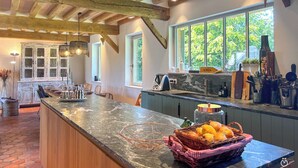 A kitchen with a marble countertop, wooden beams, and large windows offering a view of greenery.