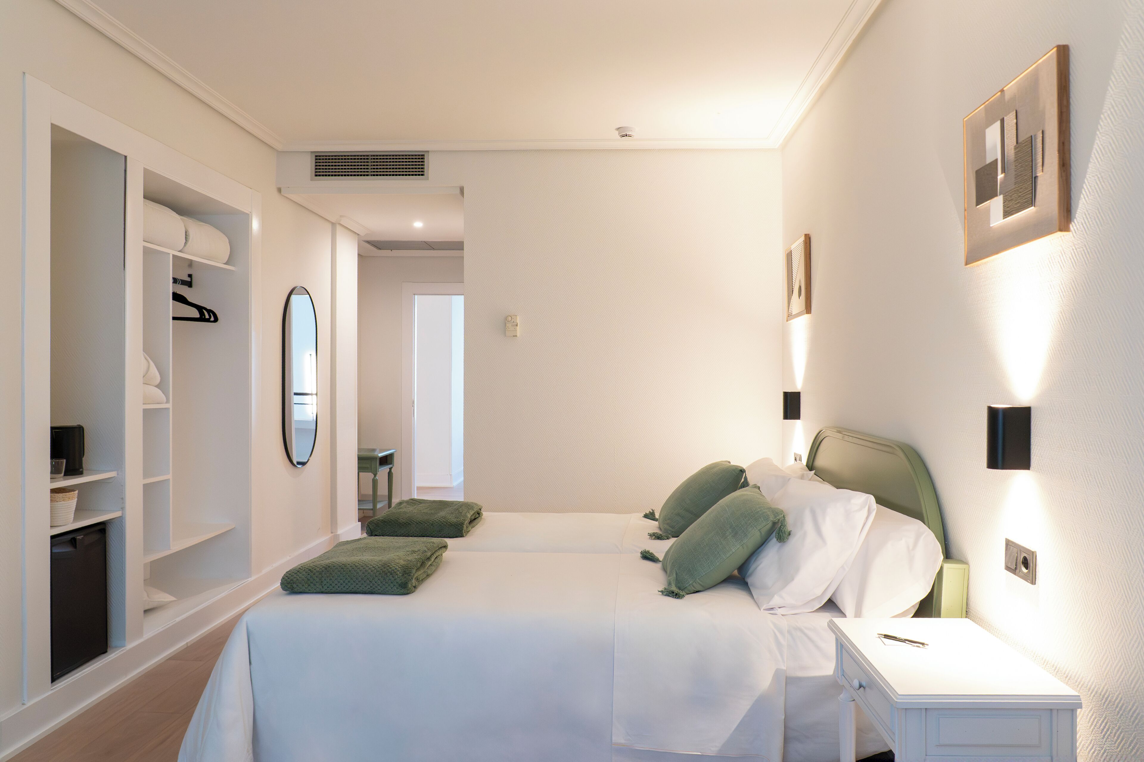 Una habitación de hotel con cama, mesitas de noche, armario y espejo.