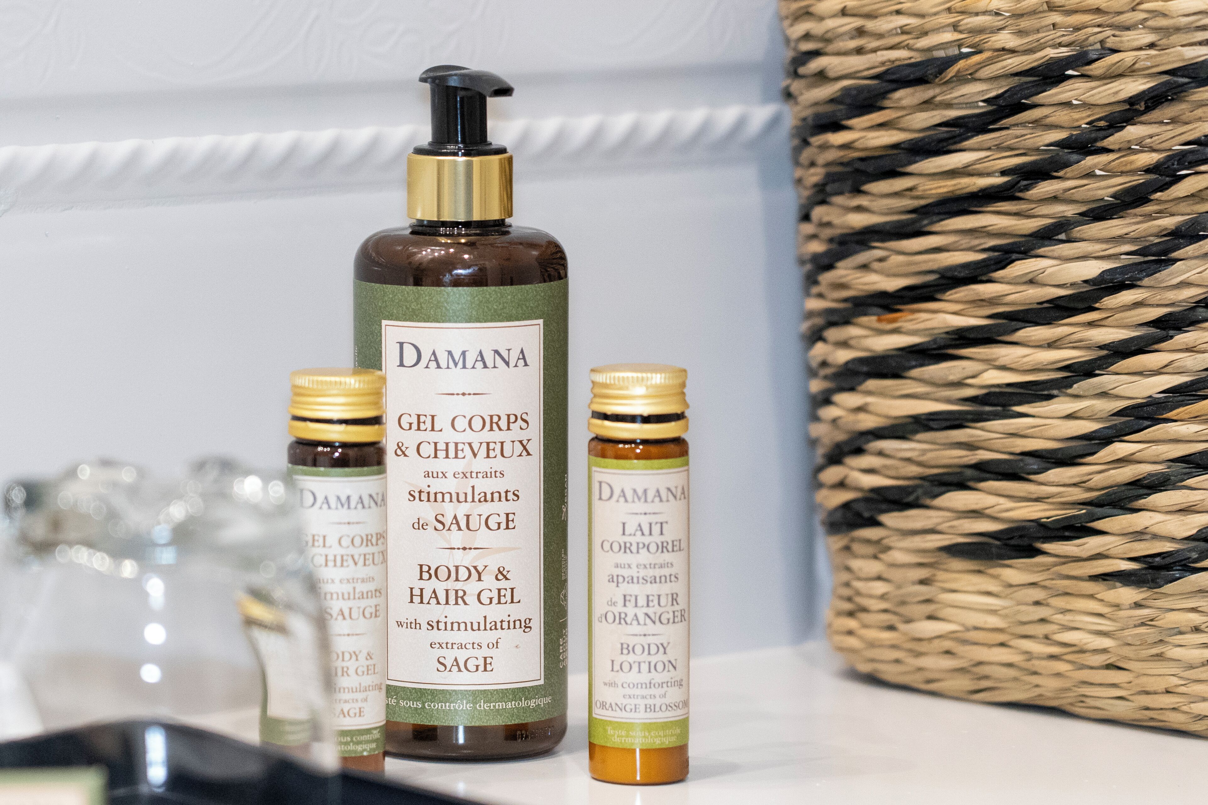 Trois flacons de gel pour le corps et les cheveux de la marque Damana, un flacon de lotion pour le corps et les cheveux de la même marque, et un panier tressé.
