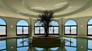 Una amplia piscina interior con una escultura de árbol central, rodeada de ventanales arqueados.