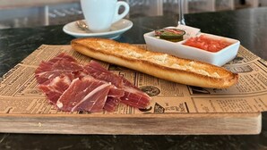 Un desayuno con un vaso de jugo de naranja, una taza de café, una baguette y un recipiente pequeño de mermelada.