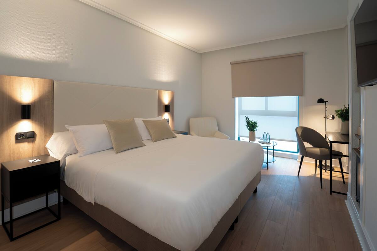 A modern bedroom with a large bed, bedside tables, a desk, and a chair.