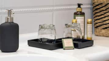 A bathroom counter with a black soap dispenser, two glass soap dishes, and a bottle of Damana soap.