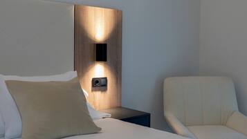 A neatly made bed with pillows, a bedside table with a wall-mounted light, and a chair.