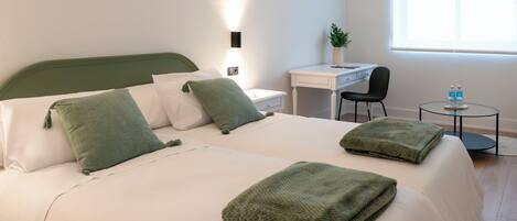 A hotel room with a bed, a desk, a chair, and a small table with bottles.