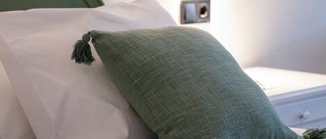 Een bed met twee kussens, één wit en één groen, en een klein fotolijstje aan de muur.