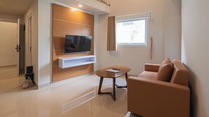 A modern living room with a flat-screen TV mounted on a wooden panel, a brown leather sofa, and a small wooden coffee table. - Casa Residence Bali (Kerobokan Kaja)