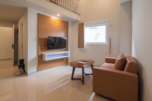 A modern living room with a flat-screen TV mounted on a wooden panel, a brown leather sofa, and a small wooden coffee table.