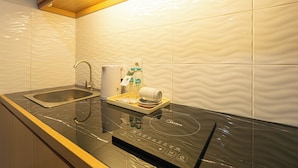 A modern kitchen with a built-in induction cooktop, a stainless steel sink, and a tray with a bottle and a cup. - Casa Residence Bali (Kerobokan Kaja)