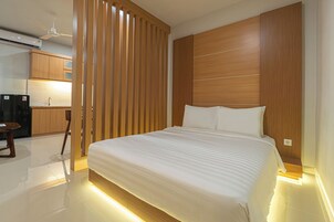 A modern hotel room with a large bed, wooden headboard, and a separate kitchenette area.