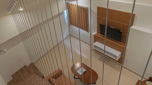 A modern interior with a wooden staircase, a TV mounted on a wooden panel, and a dining area with a table and chairs. - Casa Residence Bali (Kerobokan Kaja)