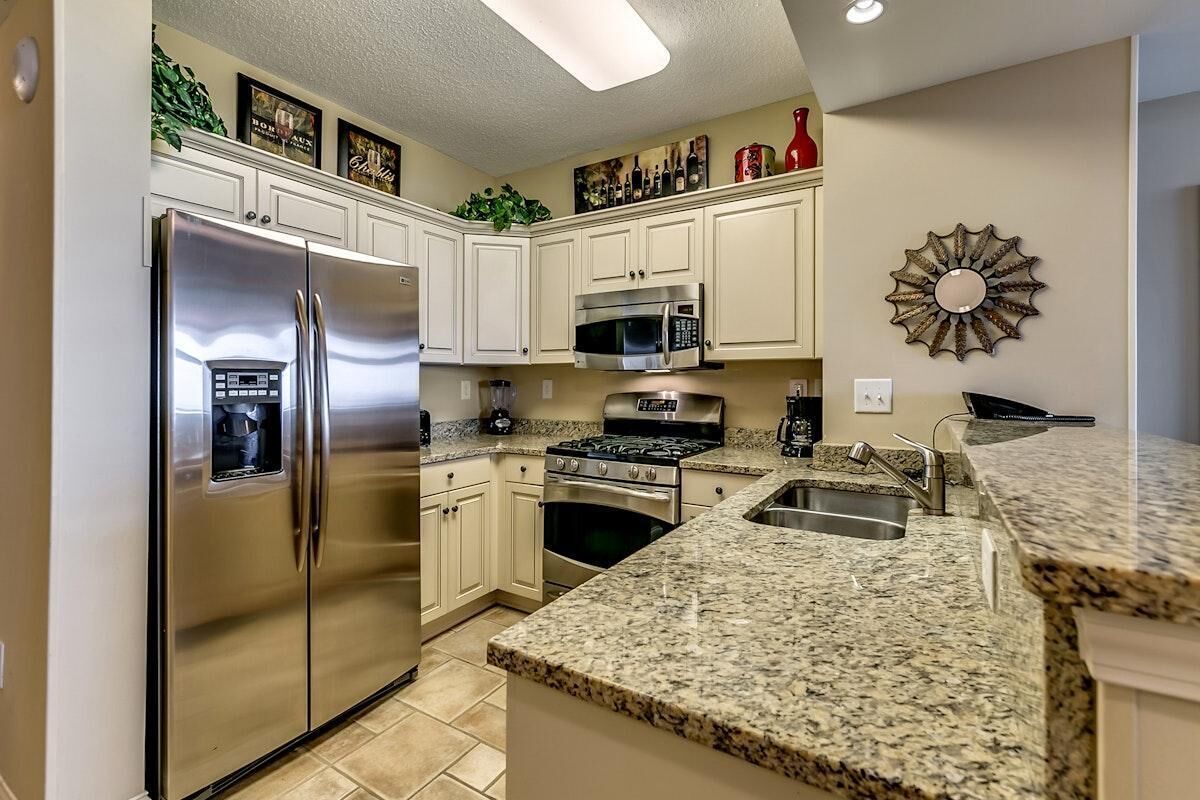 Una cocina con armarios blancos, electrodomésticos de acero inoxidable, encimeras de granito y un elemento decorativo en la pared.