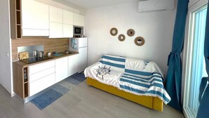 A compact room with a kitchenette, a bed with a striped blanket, and a window with curtains.
