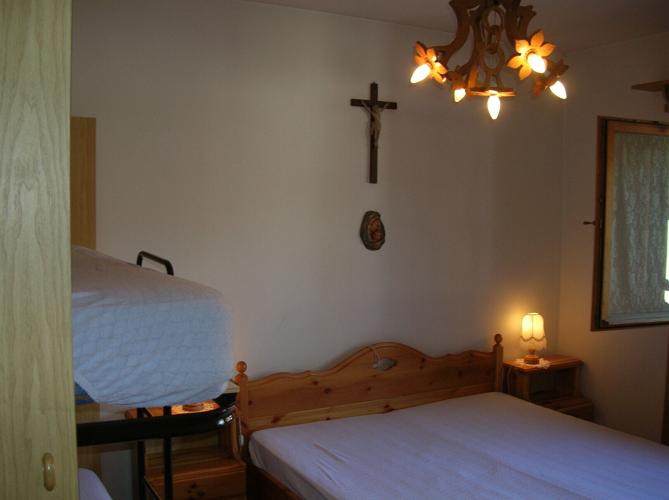 Una camera da letto con un letto in legno, un comodino con una lampada, una croce appesa al muro e un lampadario.