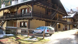 Ein traditionelles Chalet mit Holzbalkon und einer Treppe, die zum Obergeschoss führt, mit einem Auto davor.