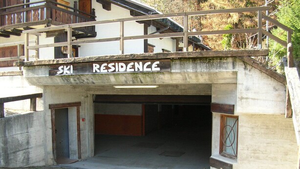 Der Eingang eines Ski-Residenzgebäudes mit einer Holztreppe, einer Betonfassade und einem Schild über dem Eingang.