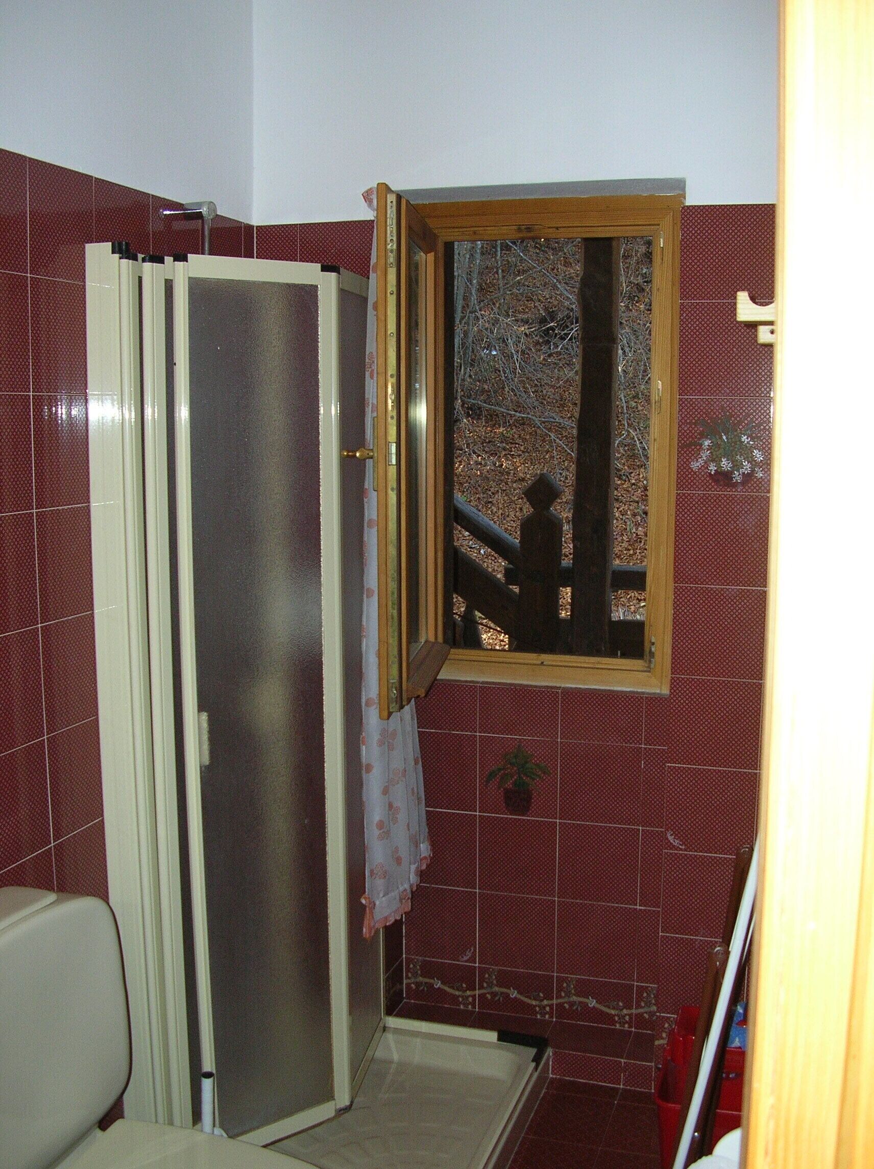 Un baño con ducha, inodoro y ventana con vistas a árboles.