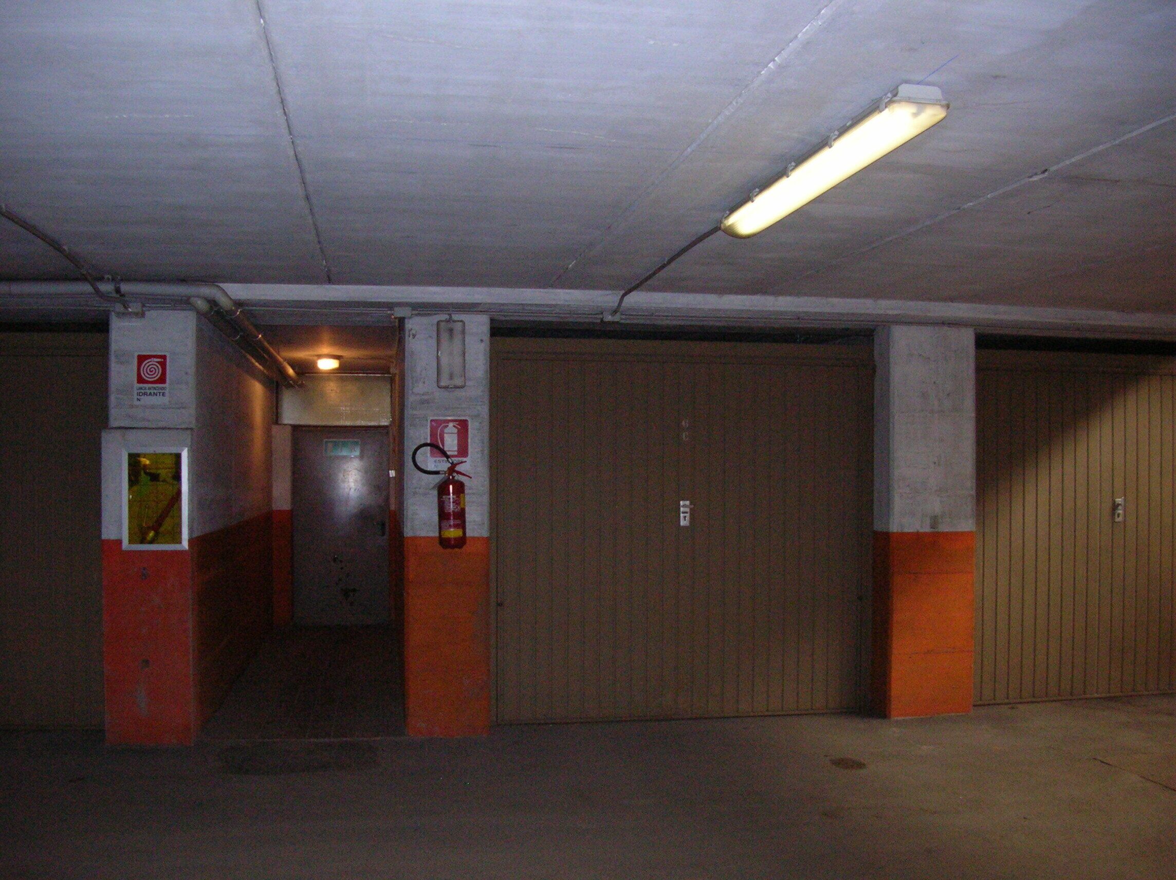 Un estacionamiento con pilares de hormigón, un extintor y una luminaria fluorescente.