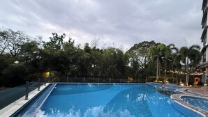A swimming pool with a tiled edge, surrounded by trees and a fence. - Room-executive Suites Bellagio Golf View (Taguig)