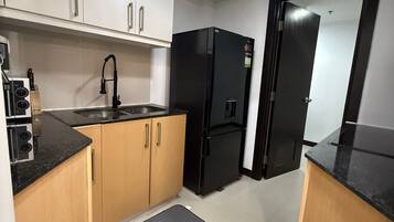 A compact kitchen with white cabinets, a black refrigerator, a sink, and a small mat on the floor.