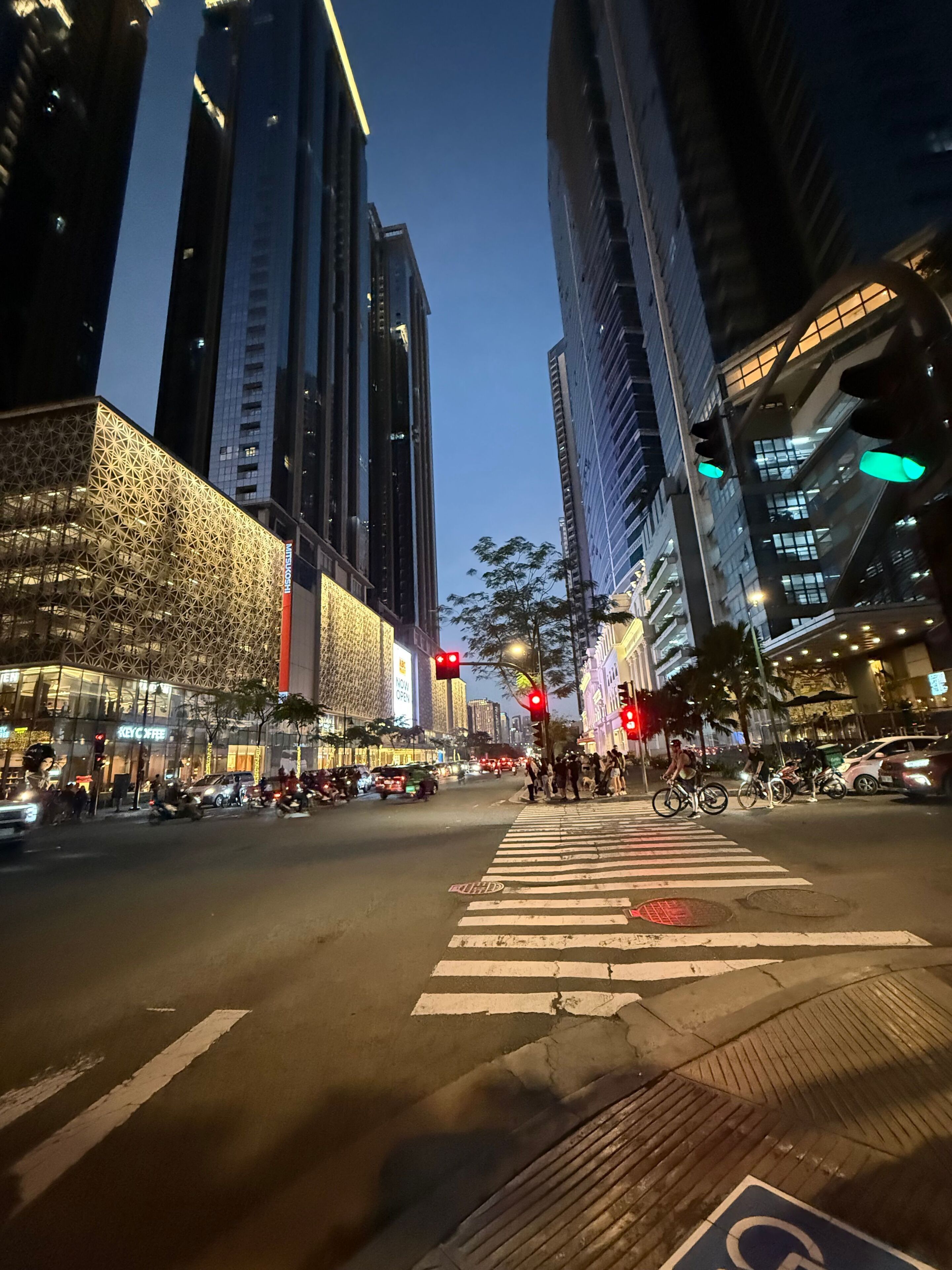 A city street at night with tall buildings, a crosswalk, and traffic lights.