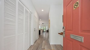 A hallway with white louvered closets, a red door with a 'No Smoking' sign, and a woven doormat on the floor.