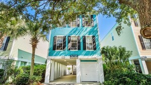 Un bâtiment à deux étages avec une façade de couleur turquoise, une entrée de garage et une enseigne indiquant « Barefoot Beach ».