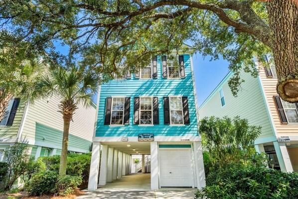 A two-story building with a teal facade, a garage entrance, and a sign reading "Barefoot Beach."