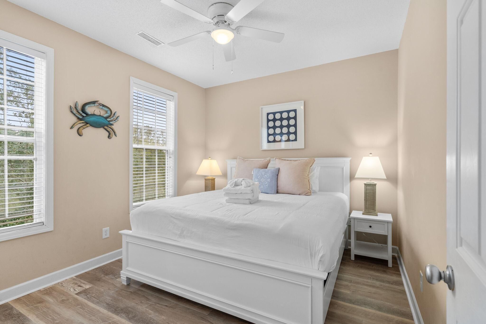 A bedroom with a large bed, two bedside tables with lamps, a ceiling fan, and a wall-mounted artwork.