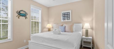 A bedroom with a large bed, two bedside tables with lamps, a ceiling fan, and a wall-mounted artwork.