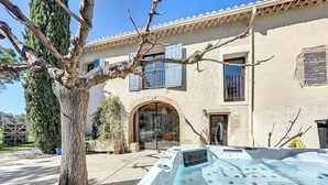 Un área de spa con un jacuzzi frente a un edificio de techo con tejas y un gran árbol.