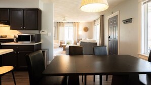 Una cocina moderna con armarios oscuros, microondas y comedor con una mesa grande y sillas.