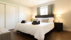 Un dormitorio con cama, mesitas de noche, ventilador de techo y una ventana con cortinas.