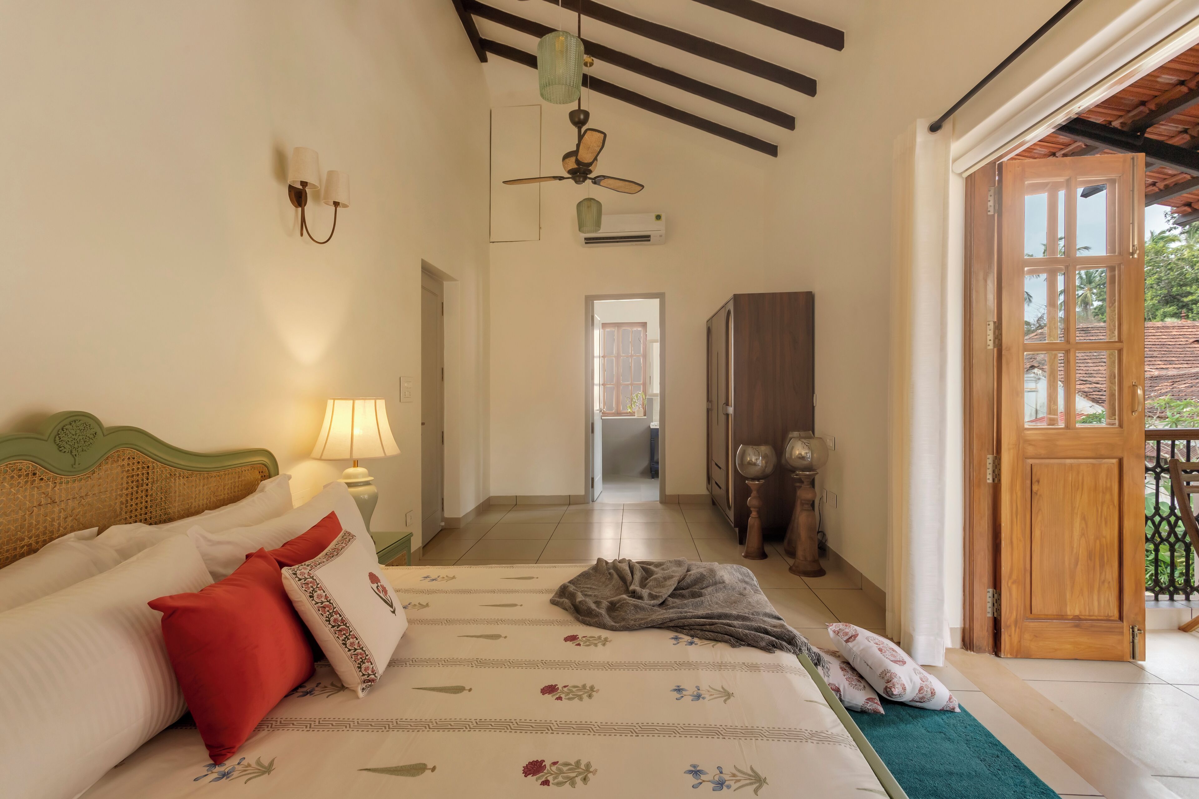 Une chambre d’hôtel avec un lit, une table de chevet avec une lampe, un ventilateur de plafond et une vue sur le balcon extérieur.