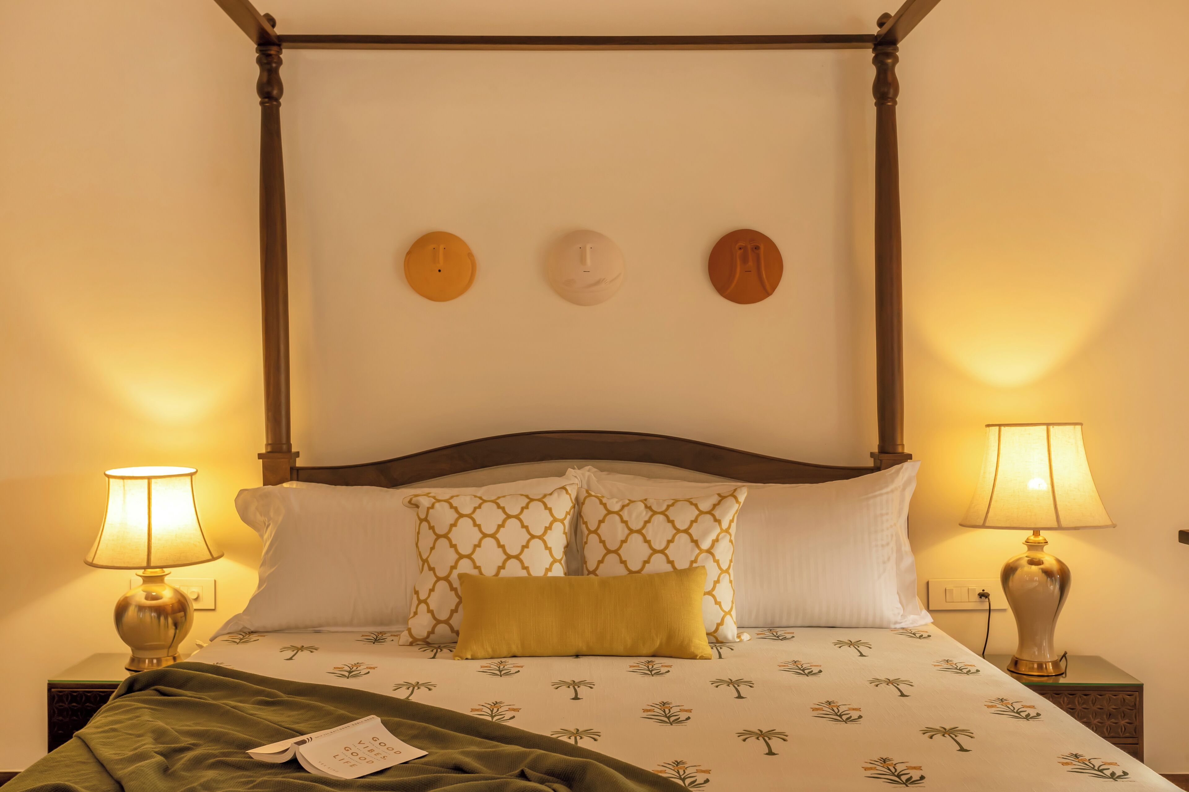 Un letto a baldacchino con un poggiatesta in legno, due abat-jour e biancheria da letto decorata.