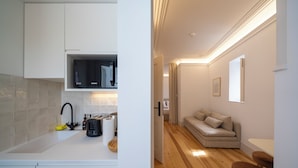 A modern kitchen with white cabinets and a built-in TV, leading to a living area with a sofa and wooden flooring. - Good Old Days (Caldas da Rainha)